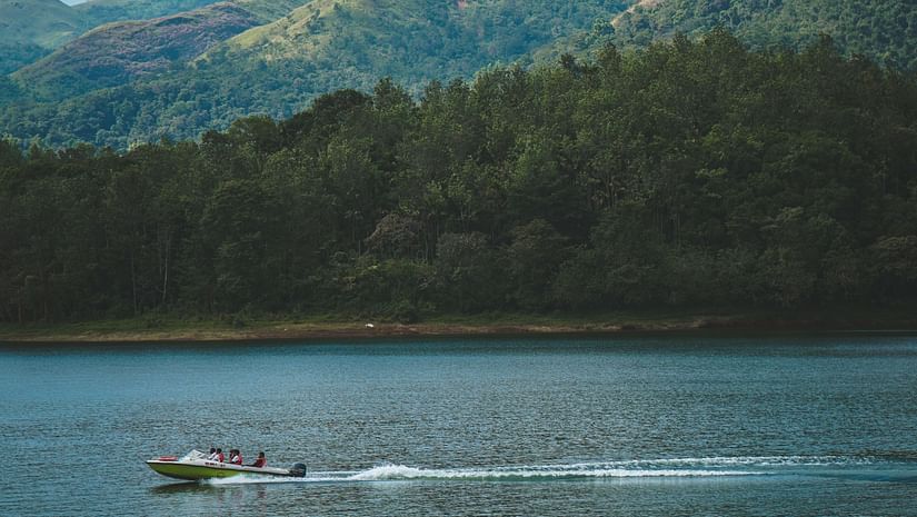 serene lake in kerela with a speedboat in a distance surrounded by green mountains