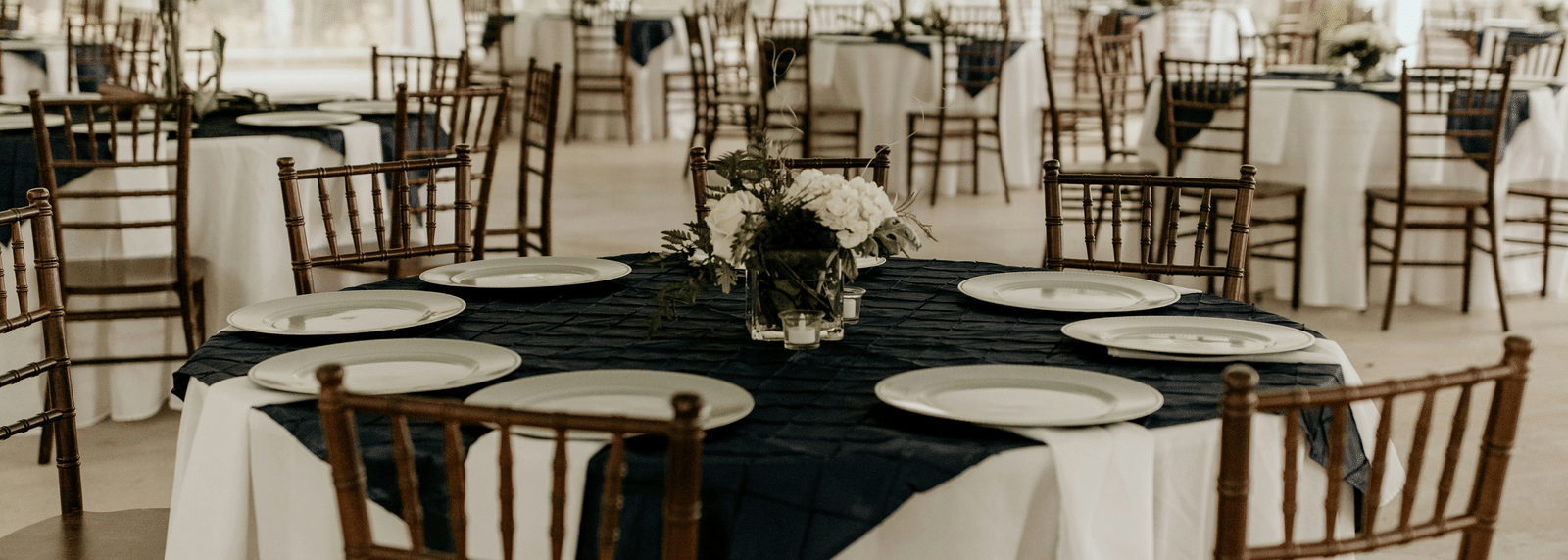 An event hall is set with white tablecloths, black runners, and dark wooden chairs.