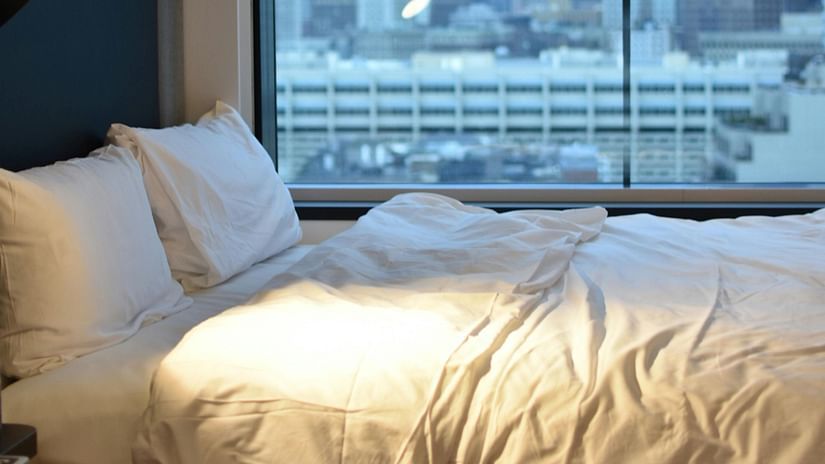 A modern hotel bedroom with a large window offering a cityscape view and a comfortable bed.