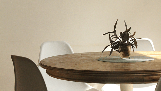 A side view of a round table with three chairs and a pot kept on the table and frame hanging on the wall
