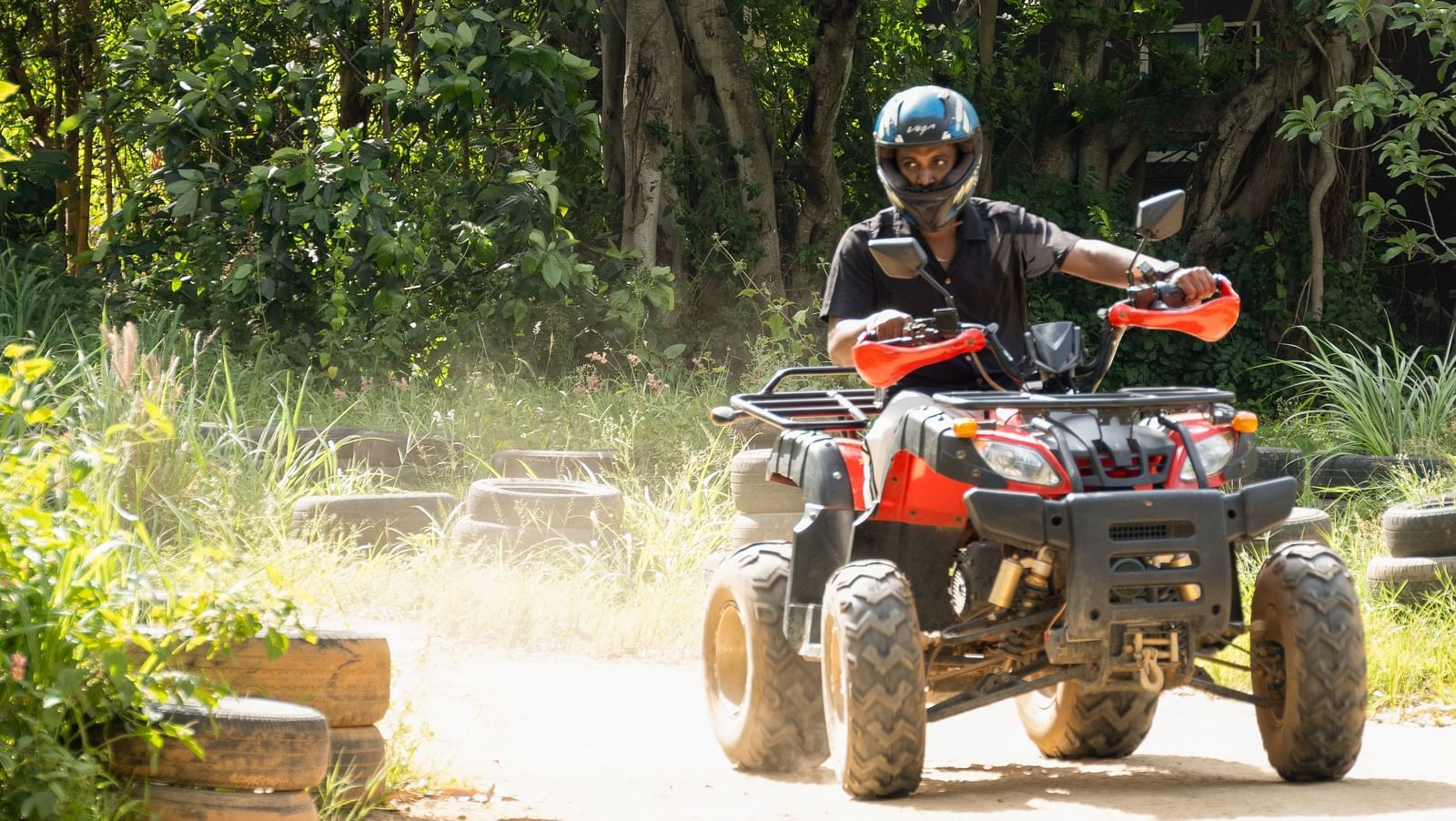 A person rides an ATV on a dirt track surrounded by trees | RD's Nature Retreat, Bangalore