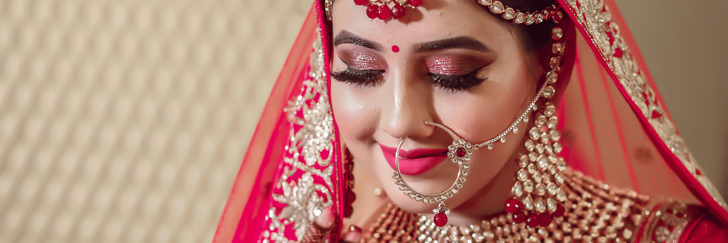 A bridal portrait featuring an Indian bride wearing an embroidered dupatta, traditional jewellery, a maang tikka, and a nath, with intricate mehendi and bridal makeup.