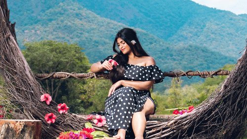 Woman sitting peacefully inside a large heart-shaped natural sculpture with mountains in the background
