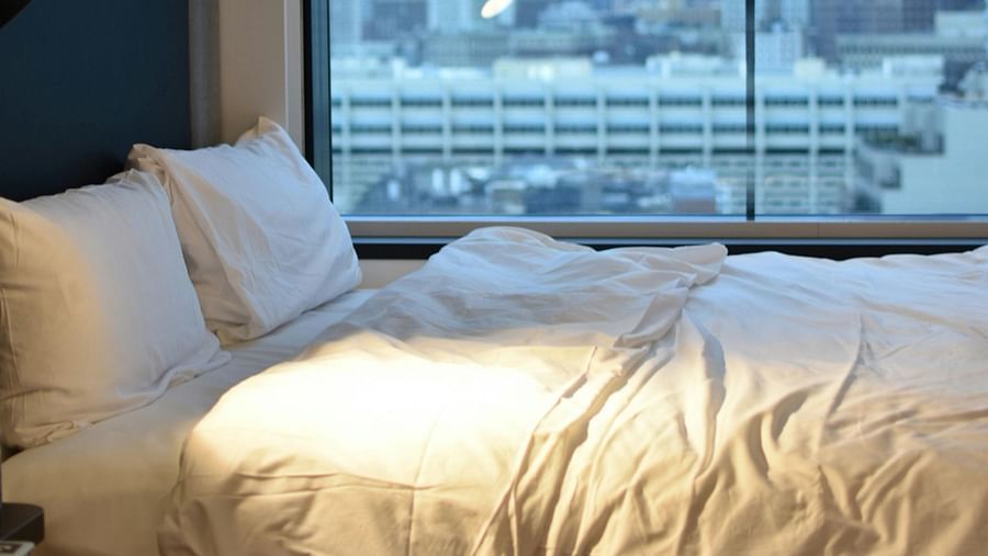 A modern hotel bedroom with a large window offering a cityscape view and a comfortable bed.