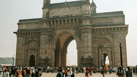 A far-out view of the Gateway of India with people walking around the courtyard in front of it. This place needs to be on top of the list on your itinerary to view the best places to see in Mumbai in 2 days.