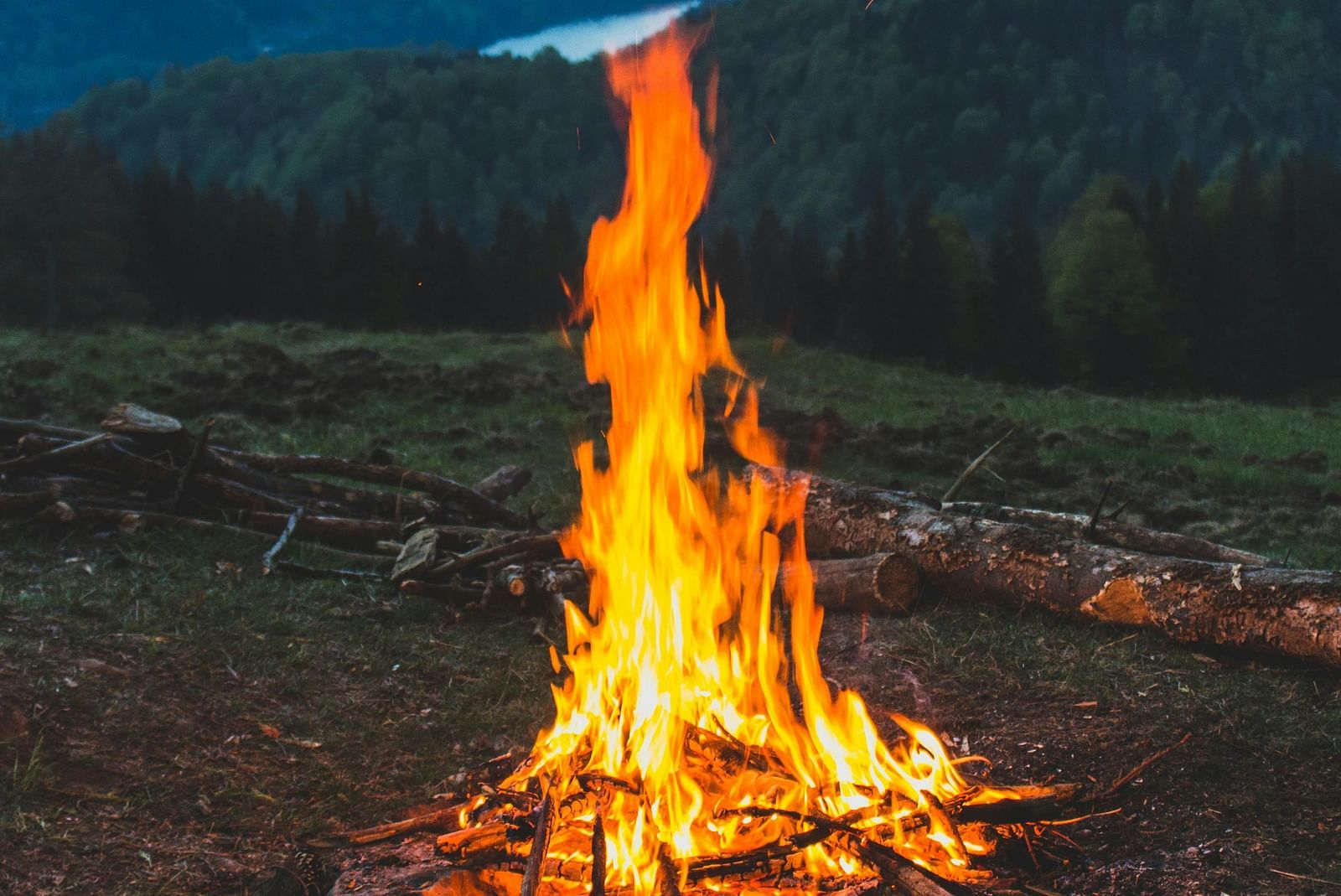 A campfire burns brightly in a mountain landscape at dusk.
