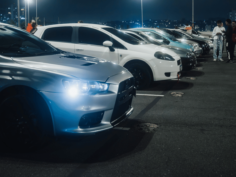 Several cars are parked closely together at night beneath the bright, harsh glare of tall street lamps.