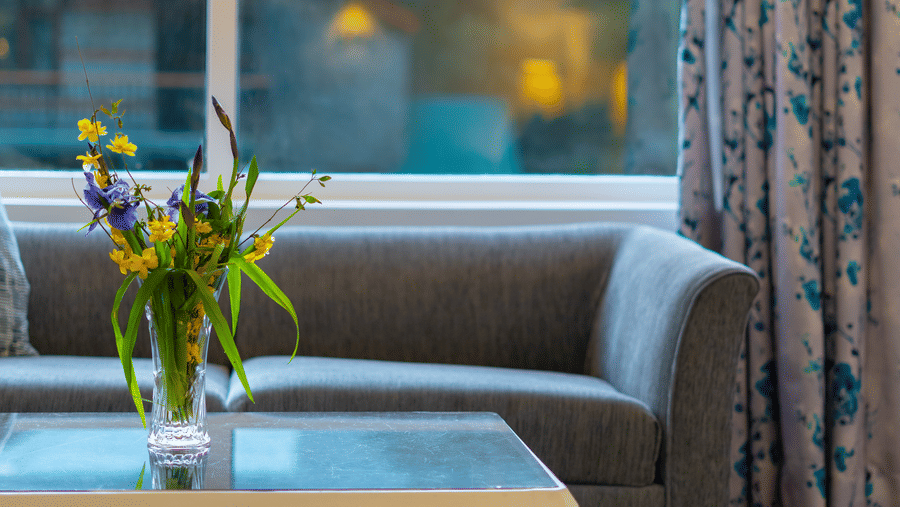 A close-up of a grey sofa and glass-top coffee table by a large window with a view of the outdoors - Johnson Lodge & Spa, Manali