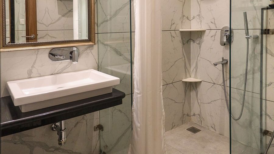 Spacious bathroom with a mirror above the washbasin and a glass panel separating the showering area | Panna Vilas Udaipur