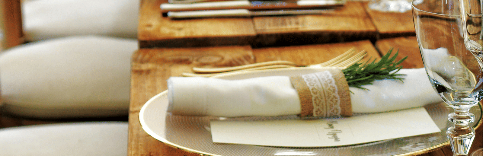 A long wooden table with beautifully set cutlery with small fern leaves in vases.