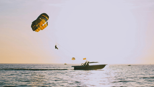 A para sail attached to a boat with a person suspended in the air above the sea.