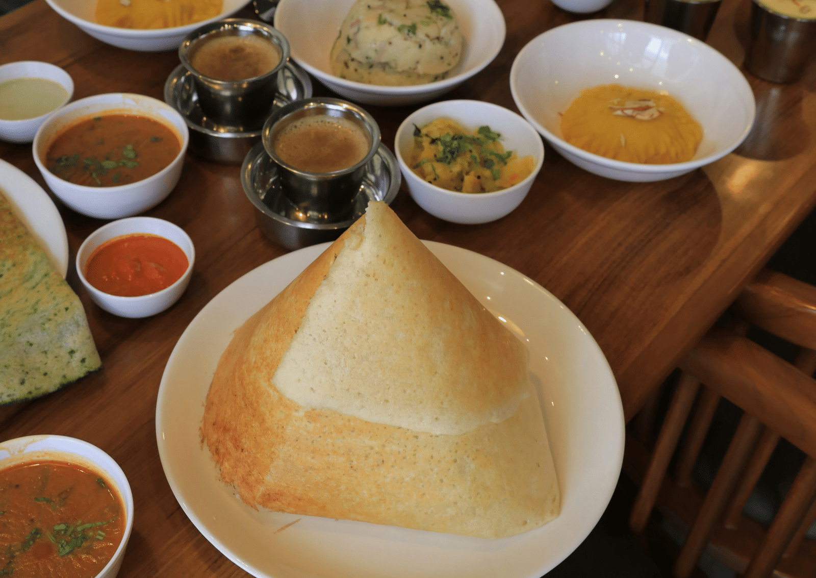 A traditional South Indian meal served on a wooden table with various curries, chutneys, sambar, and crispy dosa - Zibe Coimbatore by GRT Hotels
