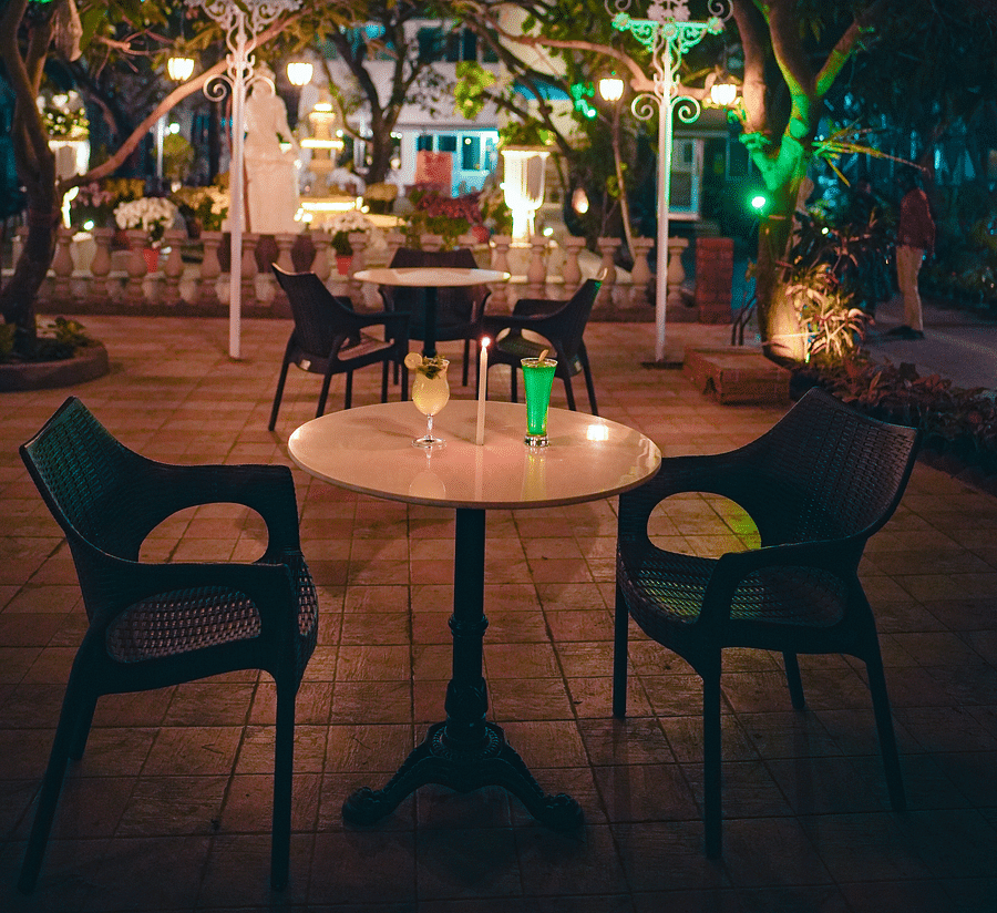An image of outdoor garden featuring table and chairs surrounded by trees and lamp shades - Rangamati Garden Resort