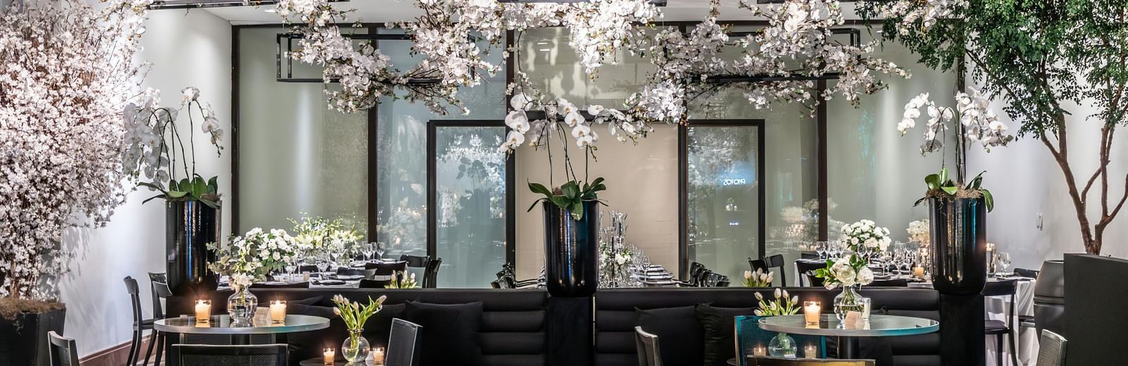 Brightly lit indoor event space with small tables, chairs, and floral decorations.