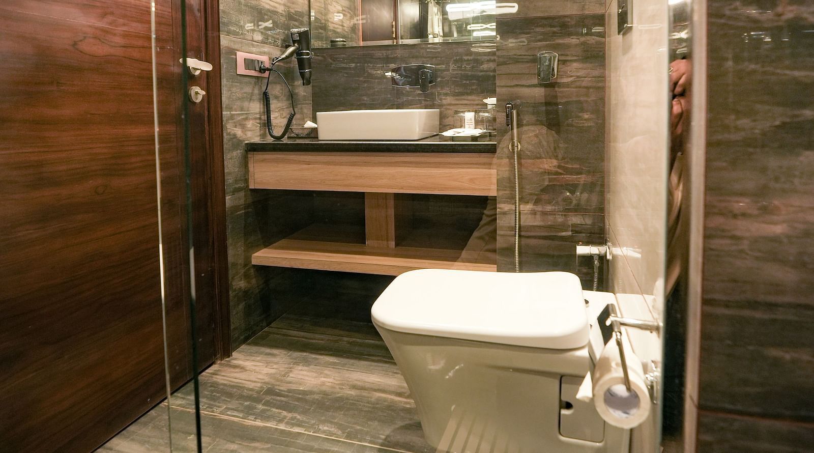 An image of a washroom with a commode and a sink placed under a wall-mounted mirror - NAMAMI BY ZENQ BANKHANDI