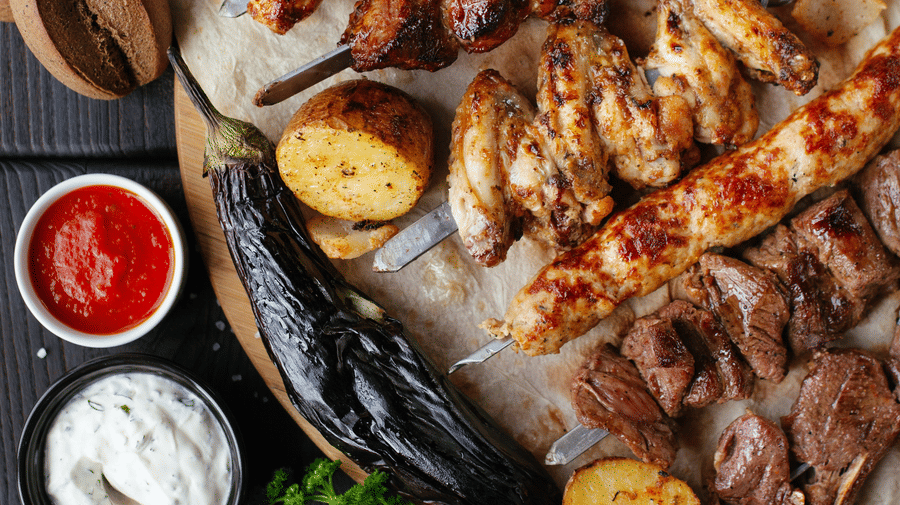 Platter of grilled kebabs served with dips and fresh vegetables.