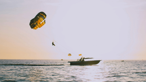 A para sail attached to a boat with a person suspended in the air above the sea.