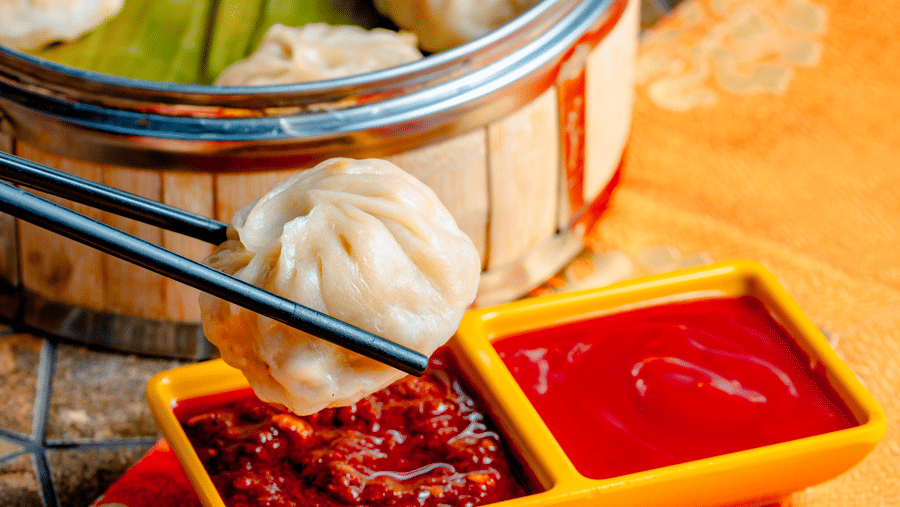A bamboo steamer filled with fresh dim sum being dipped into a spicy red sauce at Ming Dynasty, located at Noor-Us-Sabah Palace, Bhopal.