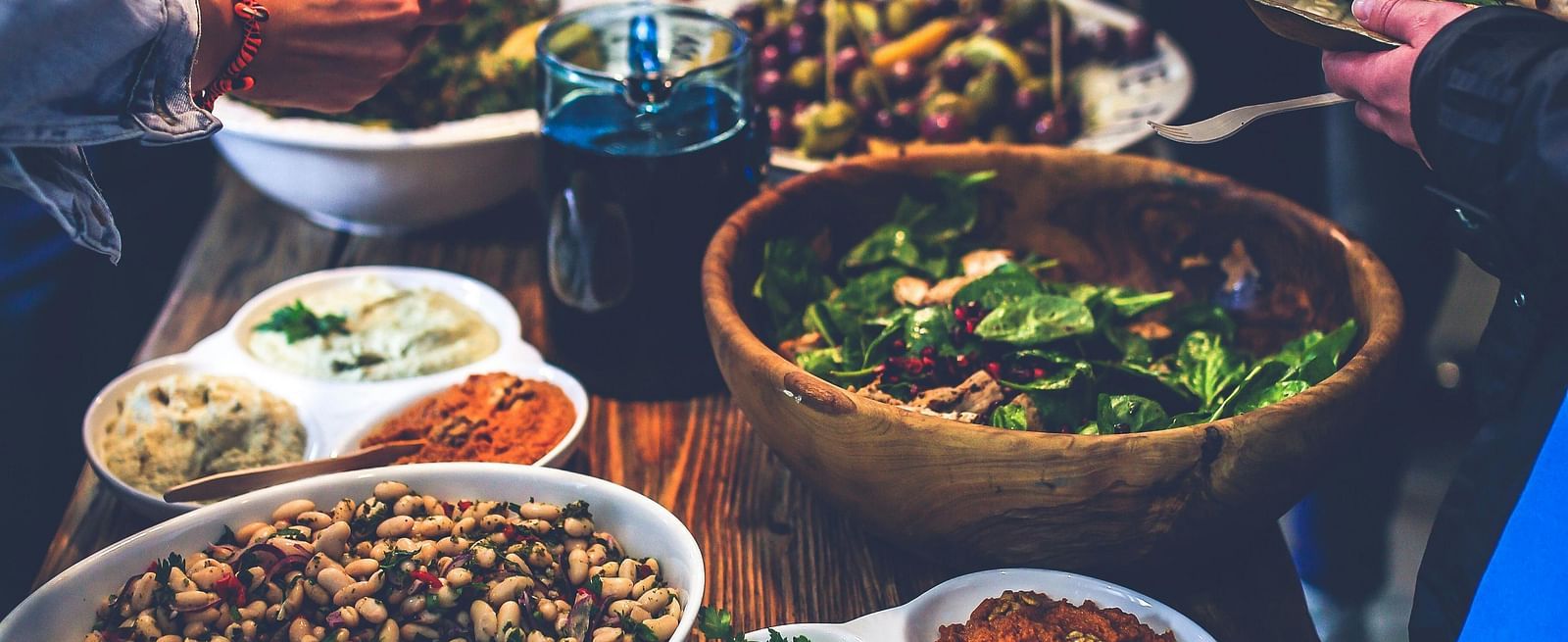 An image of a buffet table where several dishes are placed and people around are helping themselves