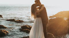 A couple embracing on top of a boulder with the ocean in the backdrop.