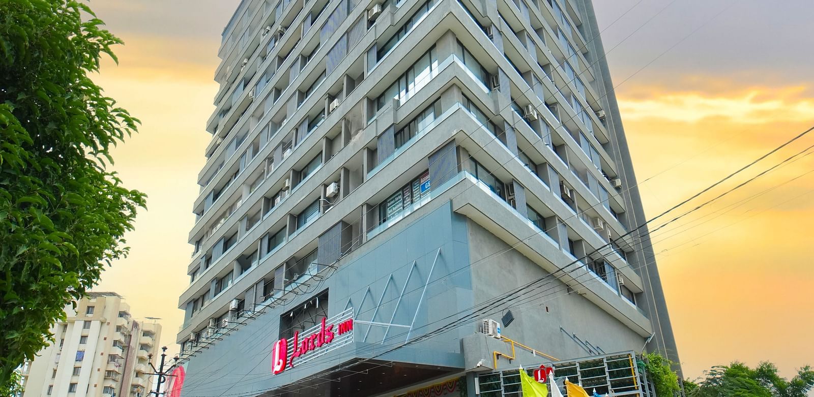 A uniquely designed triangular building with a modern facade, photographed at sunset with trees and street visible.