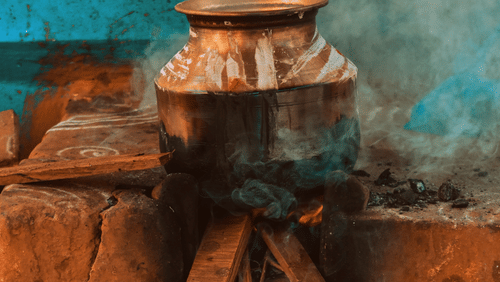 A copper Pongal pot on a earthen stove lit with wood