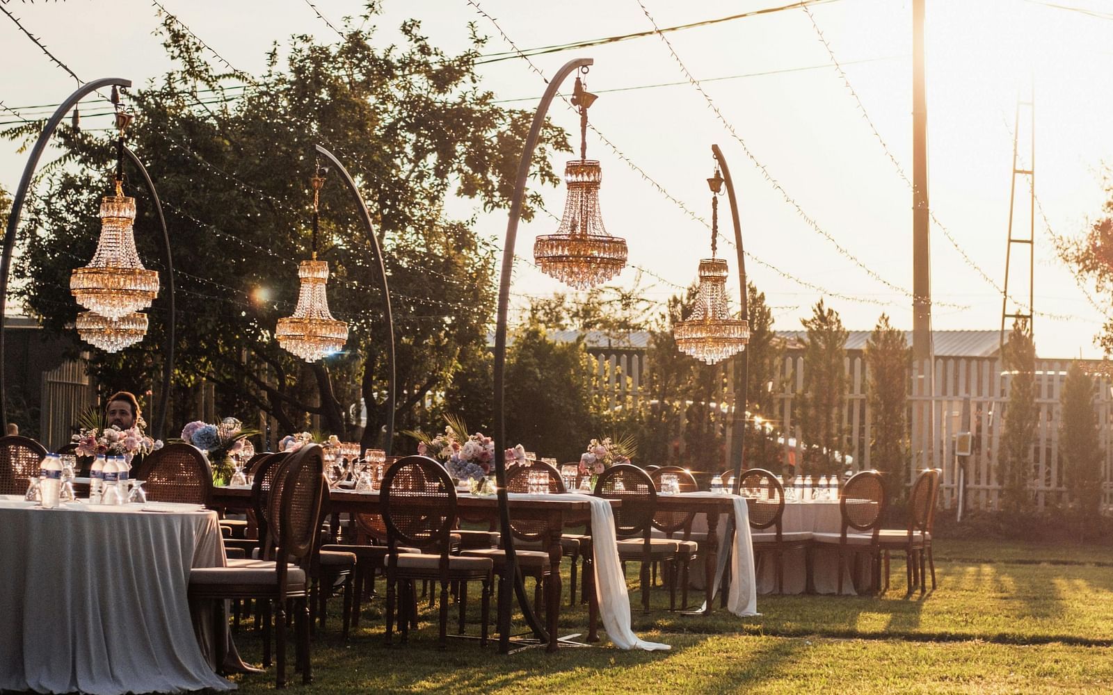 A beautiful lawn area with tall poles holding the decorative strings with a bright sun setting in the background.