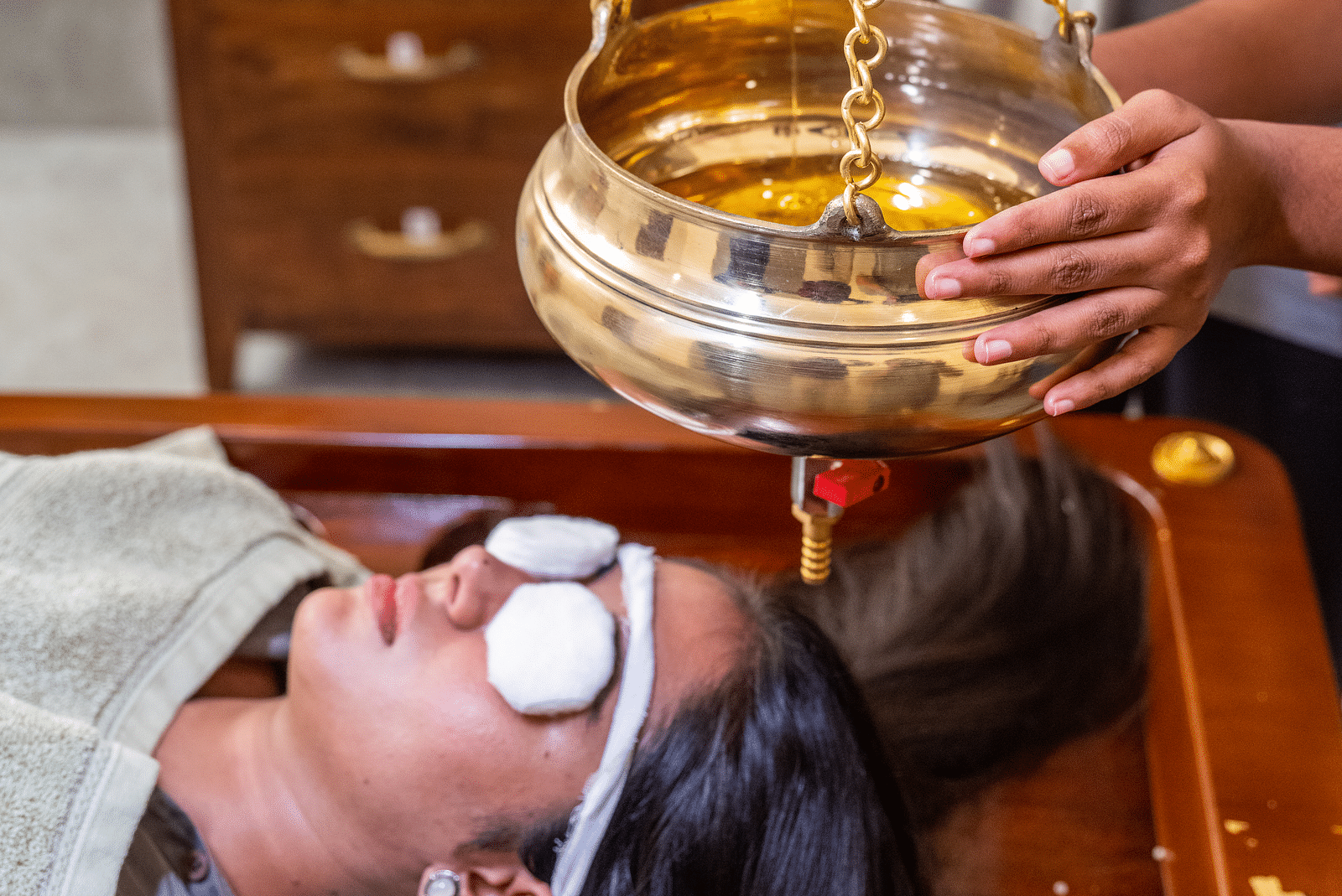 An image if a person transferring massage oil from one container to another which will be used for massage on a woman laying below it - Rajbagh Wellness