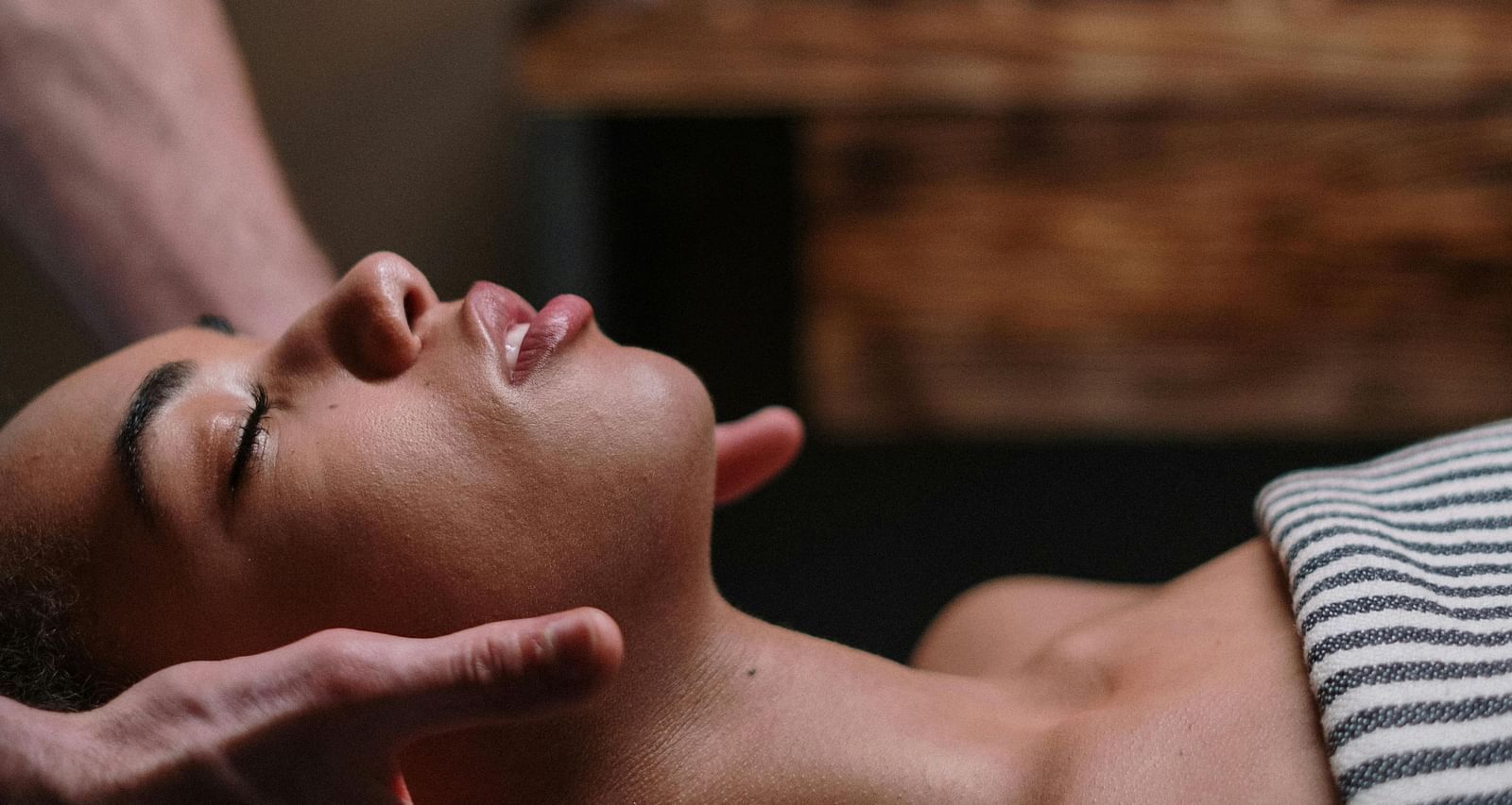 a woman with her eyes closed lying down on a bed as a masseuse massages her neck