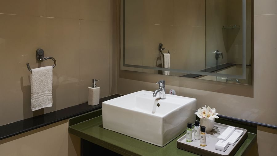 Bathroom of Super Deluxe Room with Balcony featuring a rectangular vessel sink on a dark green vanity, a large mirror, and neatly stacked white towels.