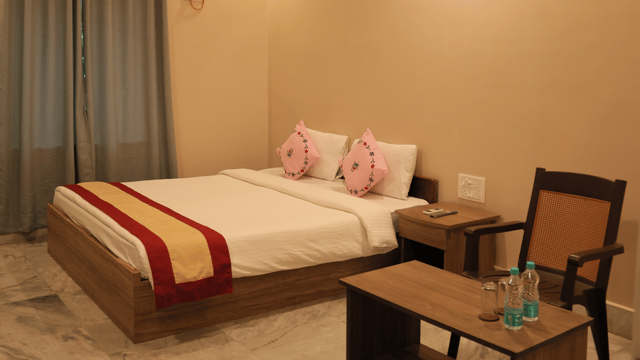 A bedroom at Shophori Wellness Retreat, Bolpur with a king size bed, a small coffee table, an armchair, air-conditioner, and a ceiling fan.