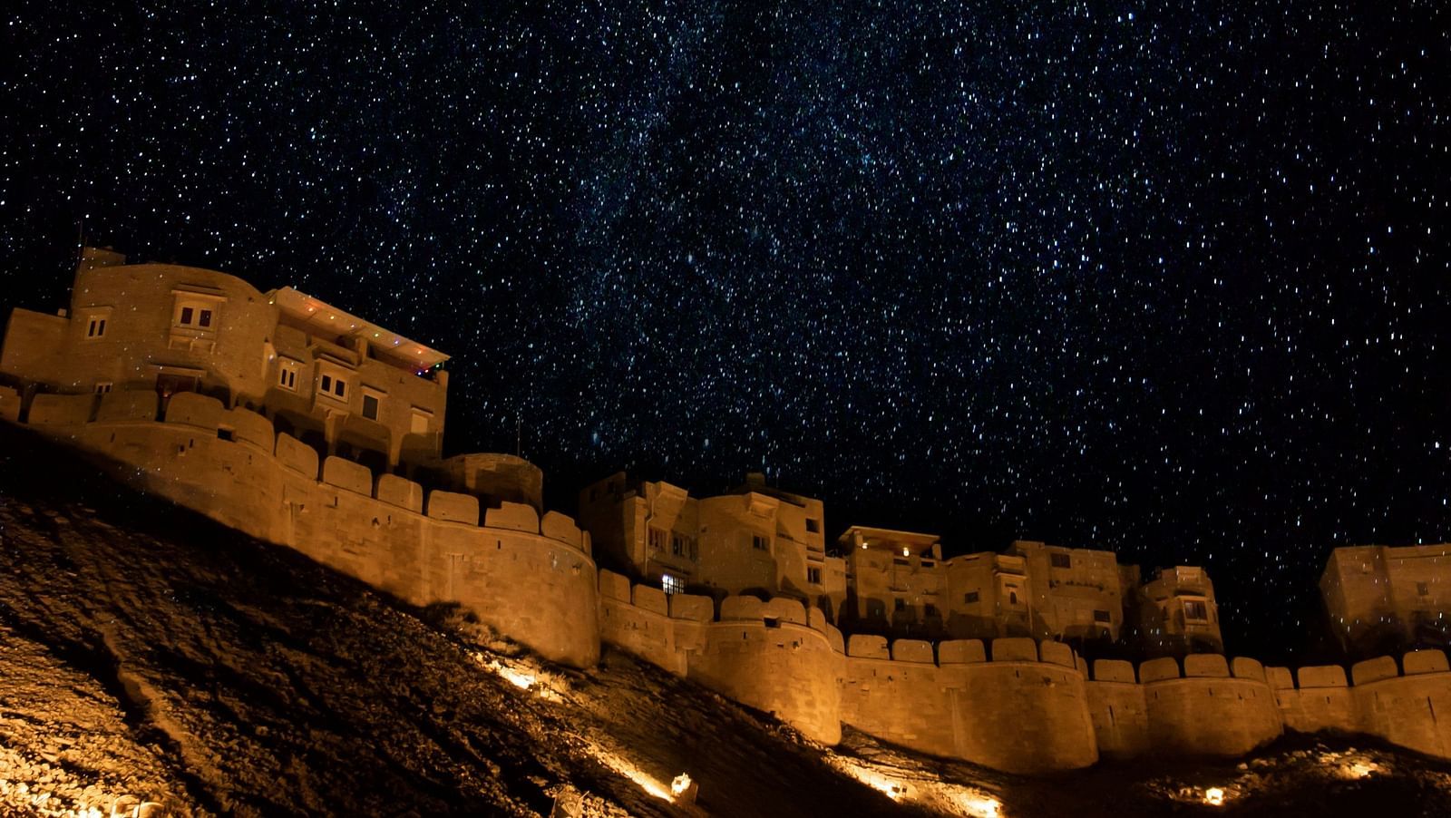 an overview of a castle as seen from below with lights on and the night sky in the background