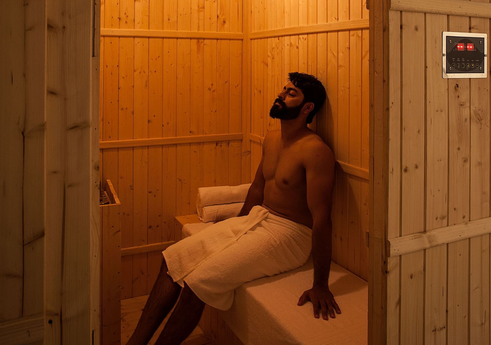 Person sitting in a wooden sauna, warm light, relaxation setting - Shreyas Retreat