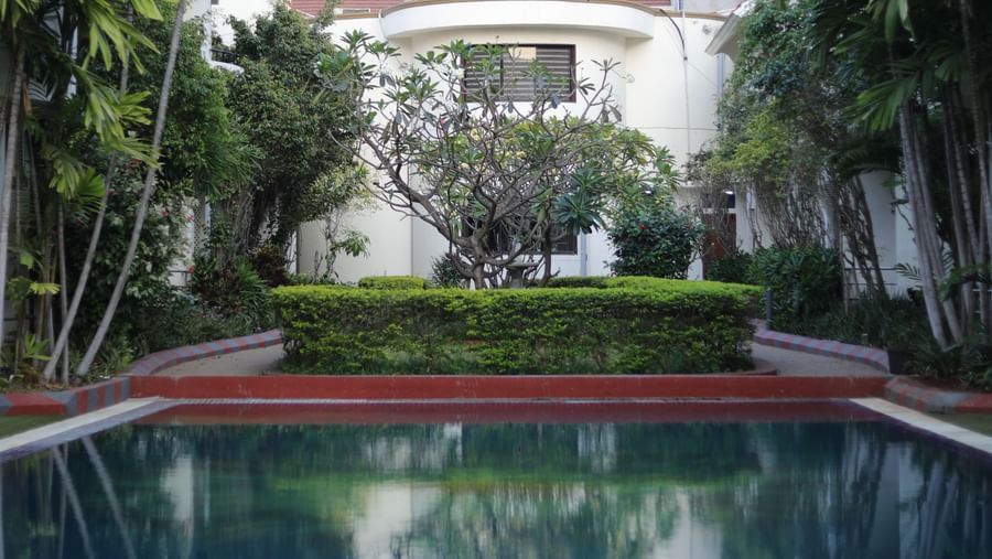 Outdoor swimming pool area with clear blue water, a small patio, and the hotel building visible in the background at Ilara Hotels & Spa, OMR, Chennai.