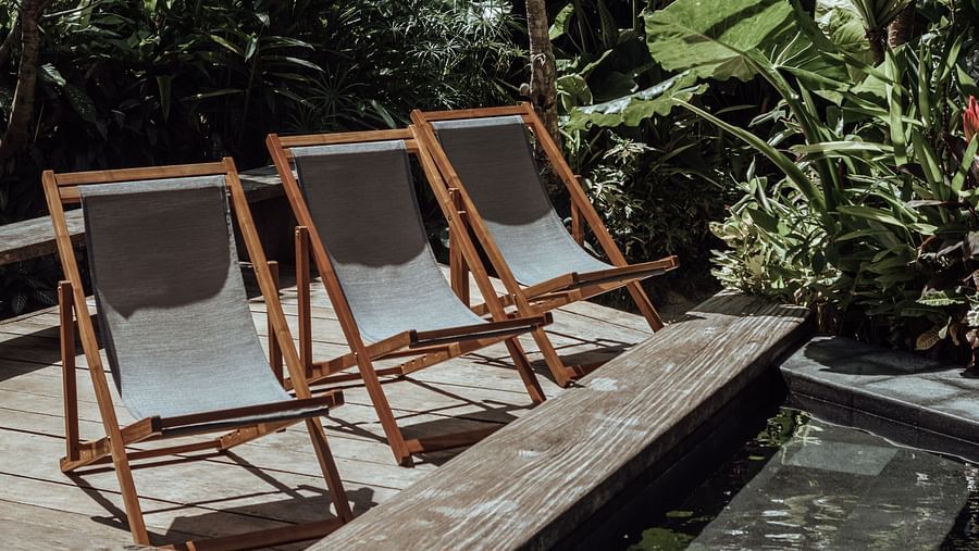 Wooden deck chairs beside a reflecting pool surrounded by lush tropical vegetation and palm trees at Lamari Siargao.
