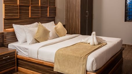A comfortable bedroom is furnished with a large bed featuring a wooden headboard, soft lighting, and a view of the room's interior | Standard Room | RD's Nature Retreat, Bangalore