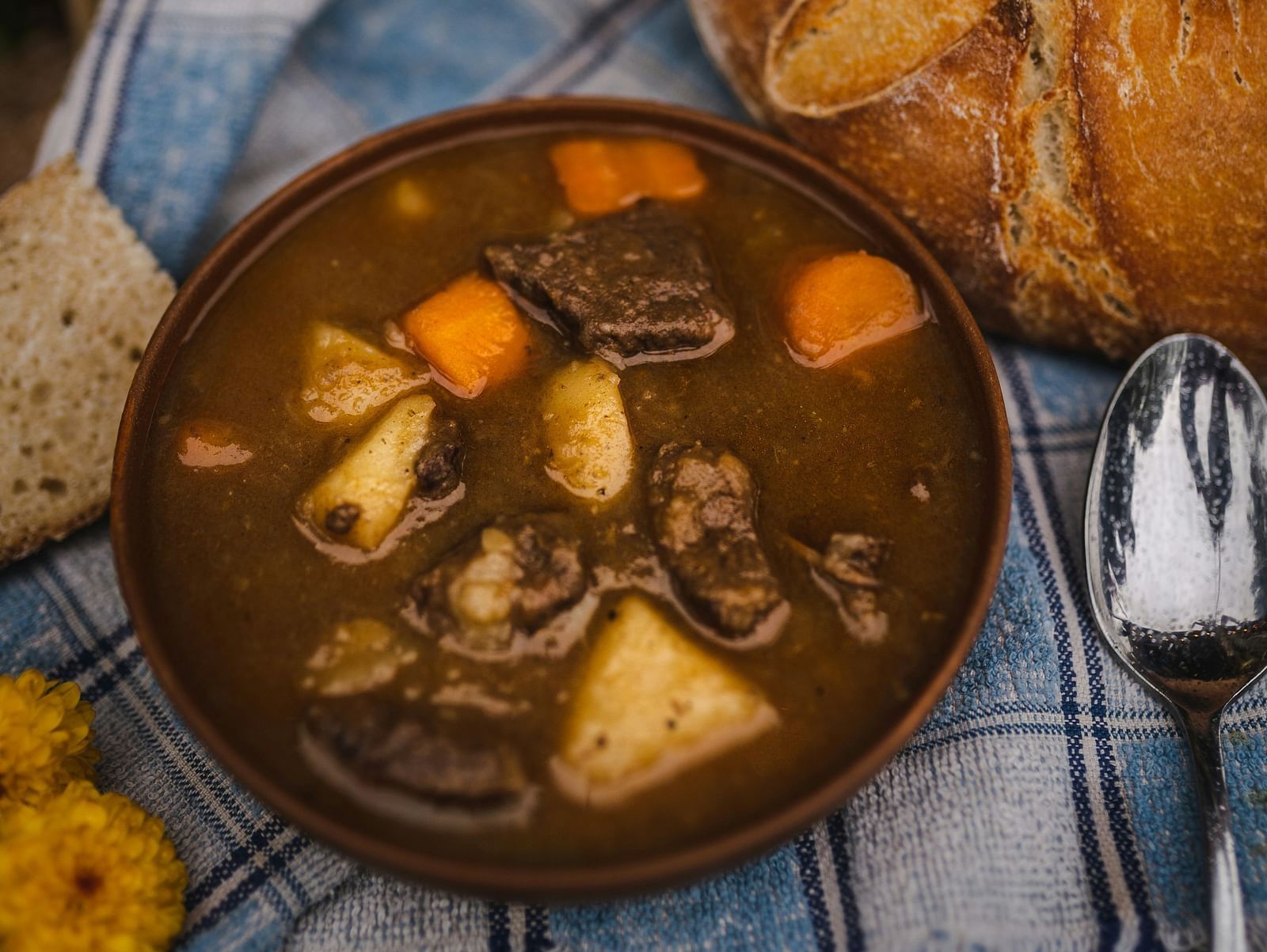 A top view of beef stew inside a bowl kept on a table with potato and carrot pieces also in view.