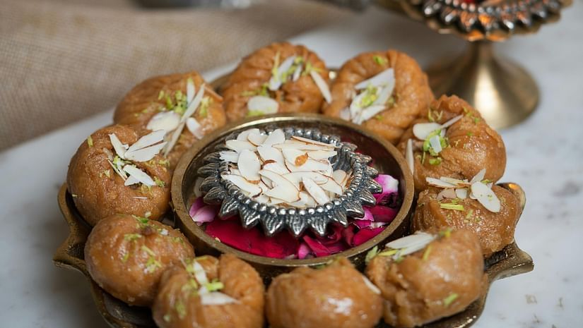 A plate of an Indian sweet placed besides a lamp and a bowl of flowers