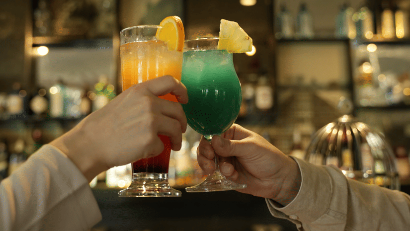 A couple of hands cheering with 2 glasses of colourful beverages at AK's Cocktail Bar at Karma Lakelands
