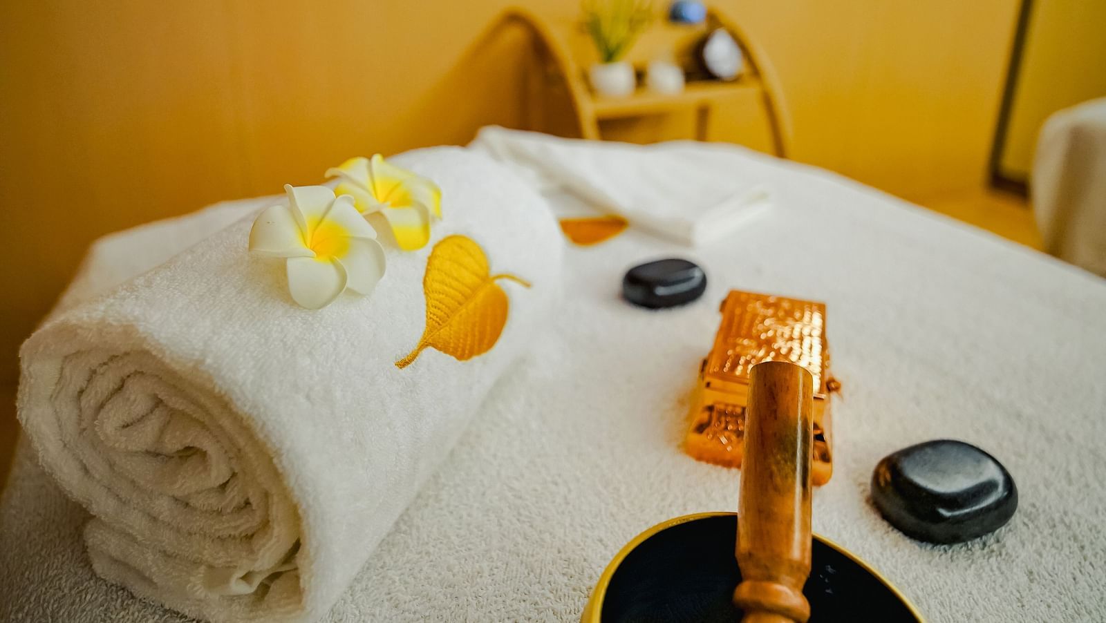 A close-up view of spa essentials, including towels and a bowl of spa products, on a massage table - Grand Madurai by GRT Hotels