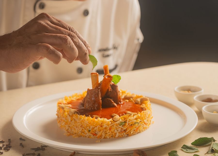 A close-up of a happy chef garnishing a meal on a plate at The Ananta Udaipur, adding final touches with a smile.