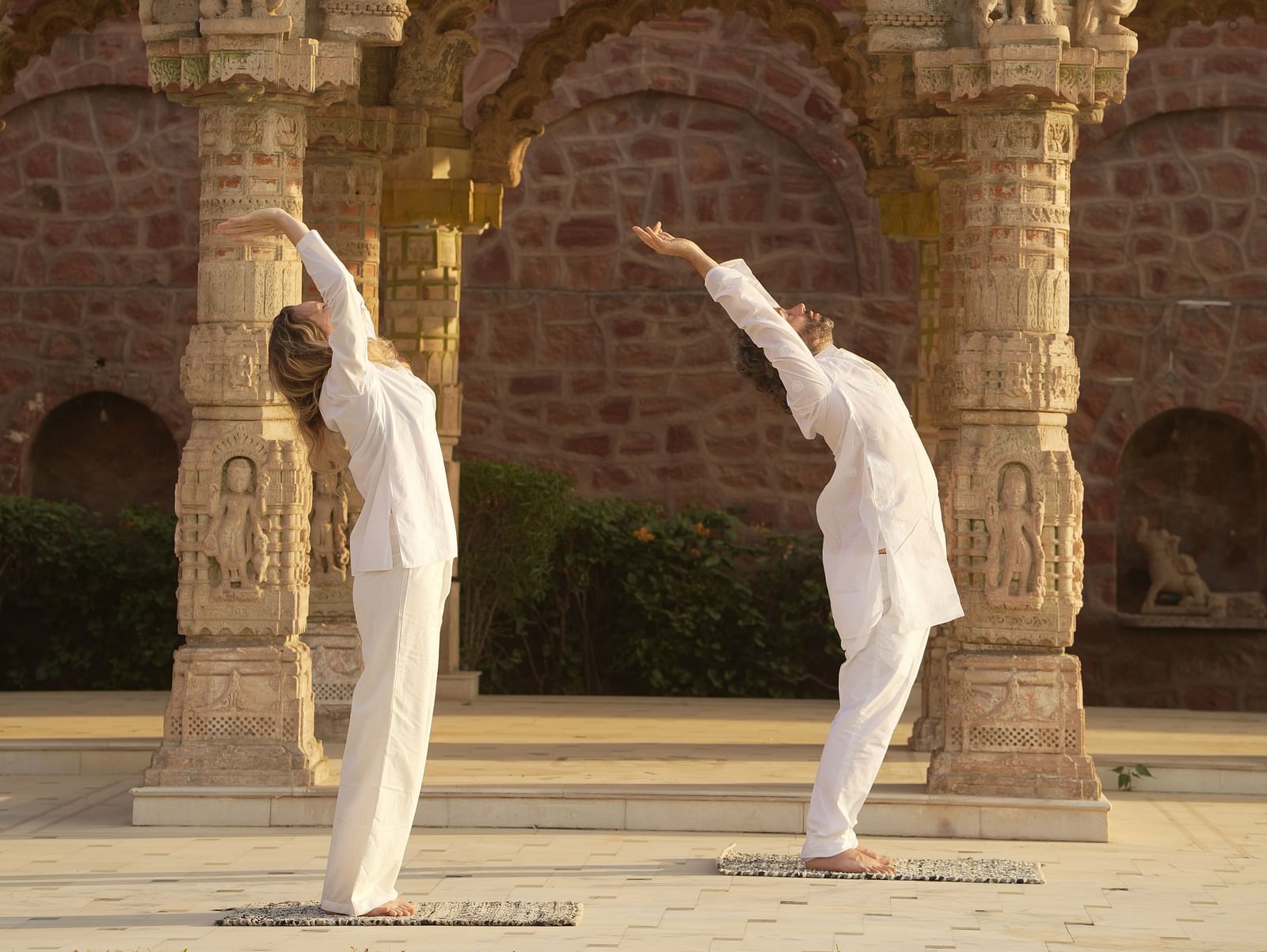 Two people stretching with a baradari in the background at Surpura Bagh.