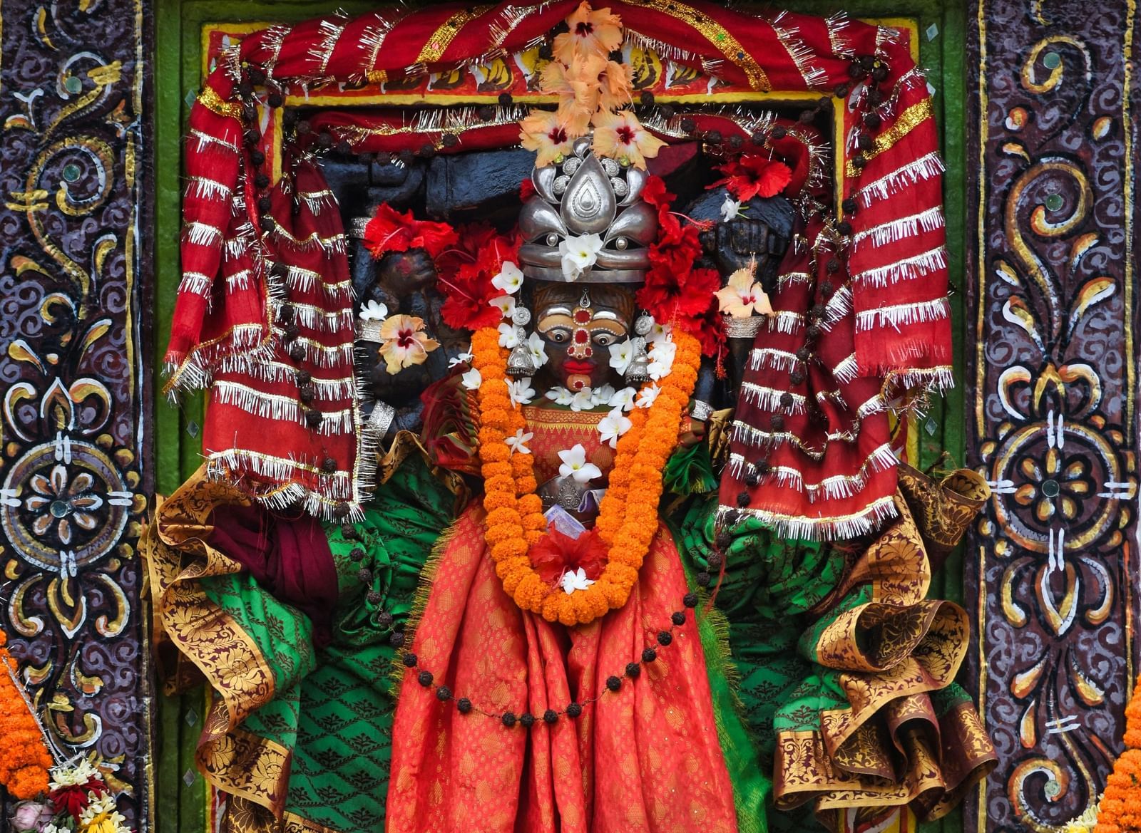 A brightly coloured idol of a Hindu deity, possibly a goddess, decorated with vibrant patterns and a floral garland.