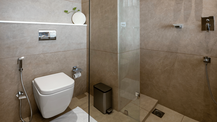 A modern bathroom showcasing a wall hung toilet, metal waste bin, and walk in shower area enclosed by a clear glass panel at Tiara by MPS.