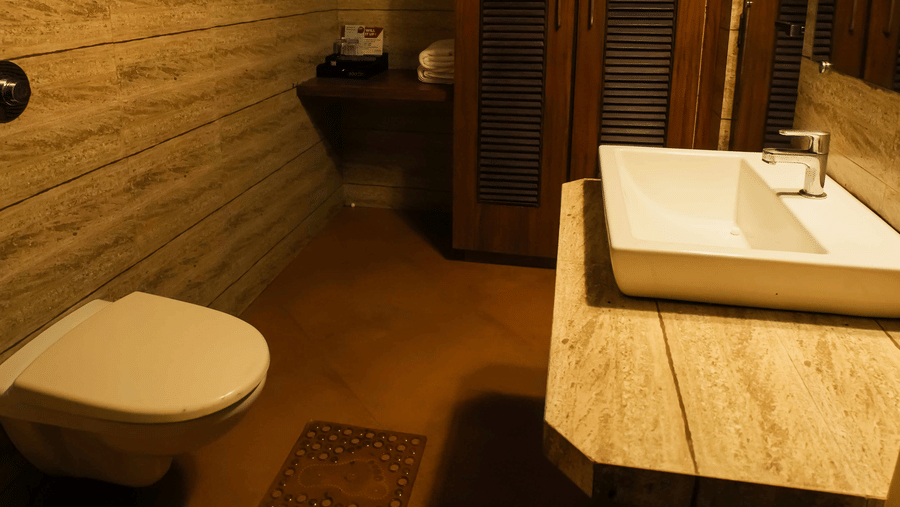 A compact washroom at Adamo The Village showcasing a countertop basin, toilet, and wooden-textured interiors.