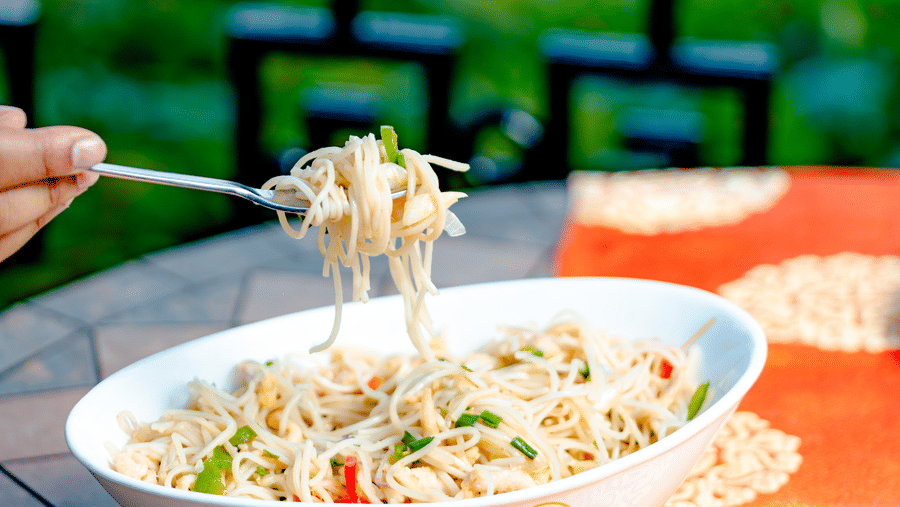 A bowl of noodles being served at Ming Dynasty, located within Noor-Us-Sabah Palace, Bhopal, presented on an outdoor table with an orange patterned runner.