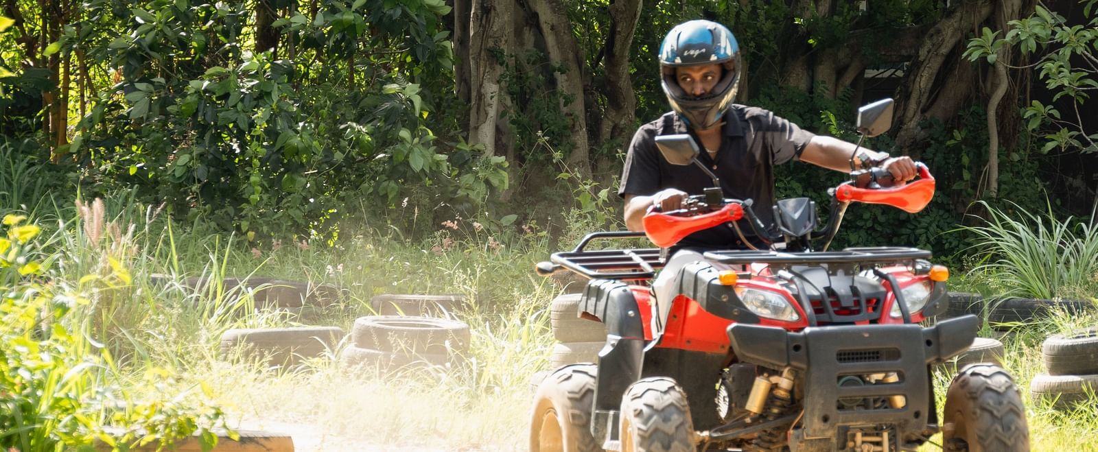 A person rides an ATV on a dirt track surrounded by trees | RD's Nature Retreat, Bangalore