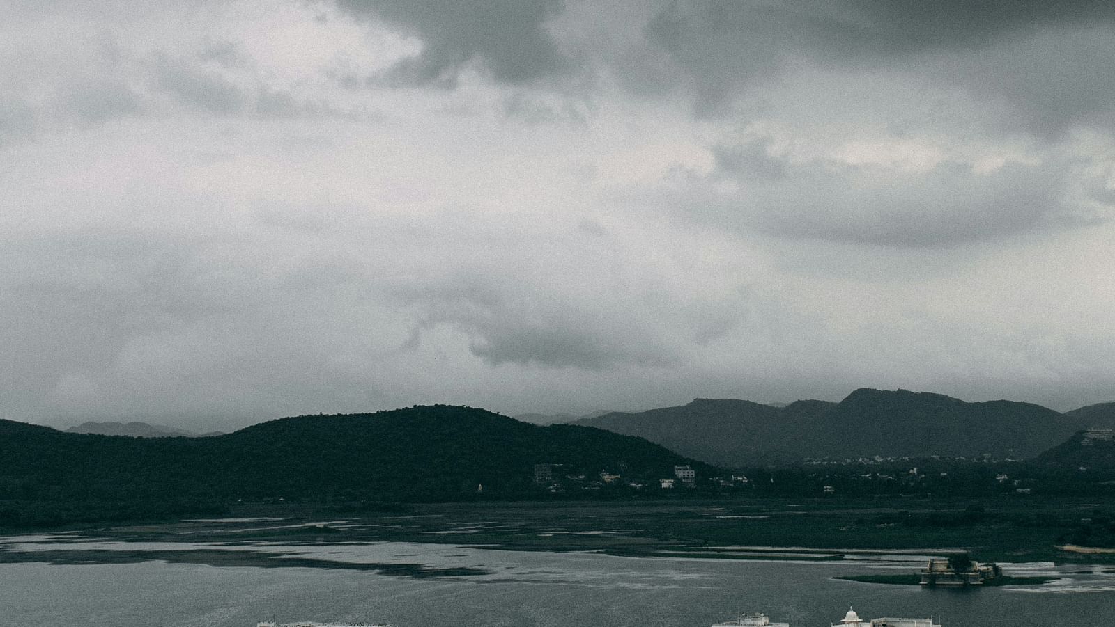 A far out view of the lake palace surrounded by the lake with rain clouds above it.