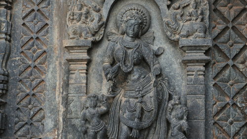 A close up of a stone carving on a wall of Hindu deity with two carvings of smaller deities next to her.