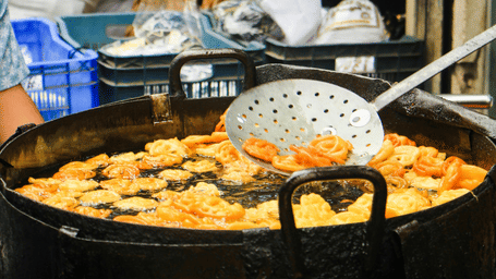 Large black pot of simmering vegetable curry being stirred with a ladle in an outdoor market.